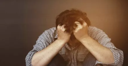 Bărbat copleșit de anxietate, cu capul în mâini.